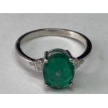A WHITE METAL RING WITH AN OVAL LABORATORY EMERALD WITH THREE CLEAR STONES TO EACH SIDE SIZE Q/R