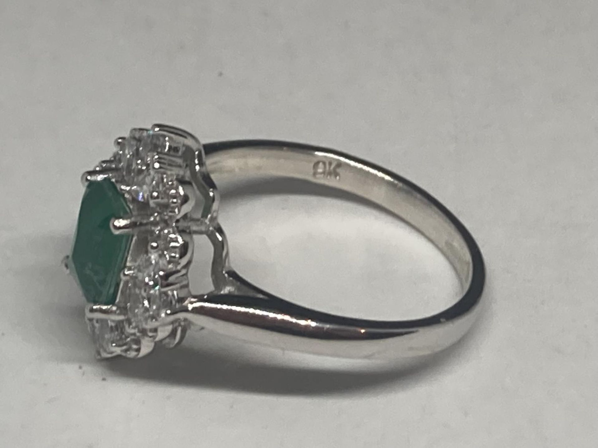 A WHITE METAL RING WITH A RECTANGULAR LABORATORY EMERALD SURROUNDED BY CLEAR STONES SIZE Q/R - Image 3 of 8