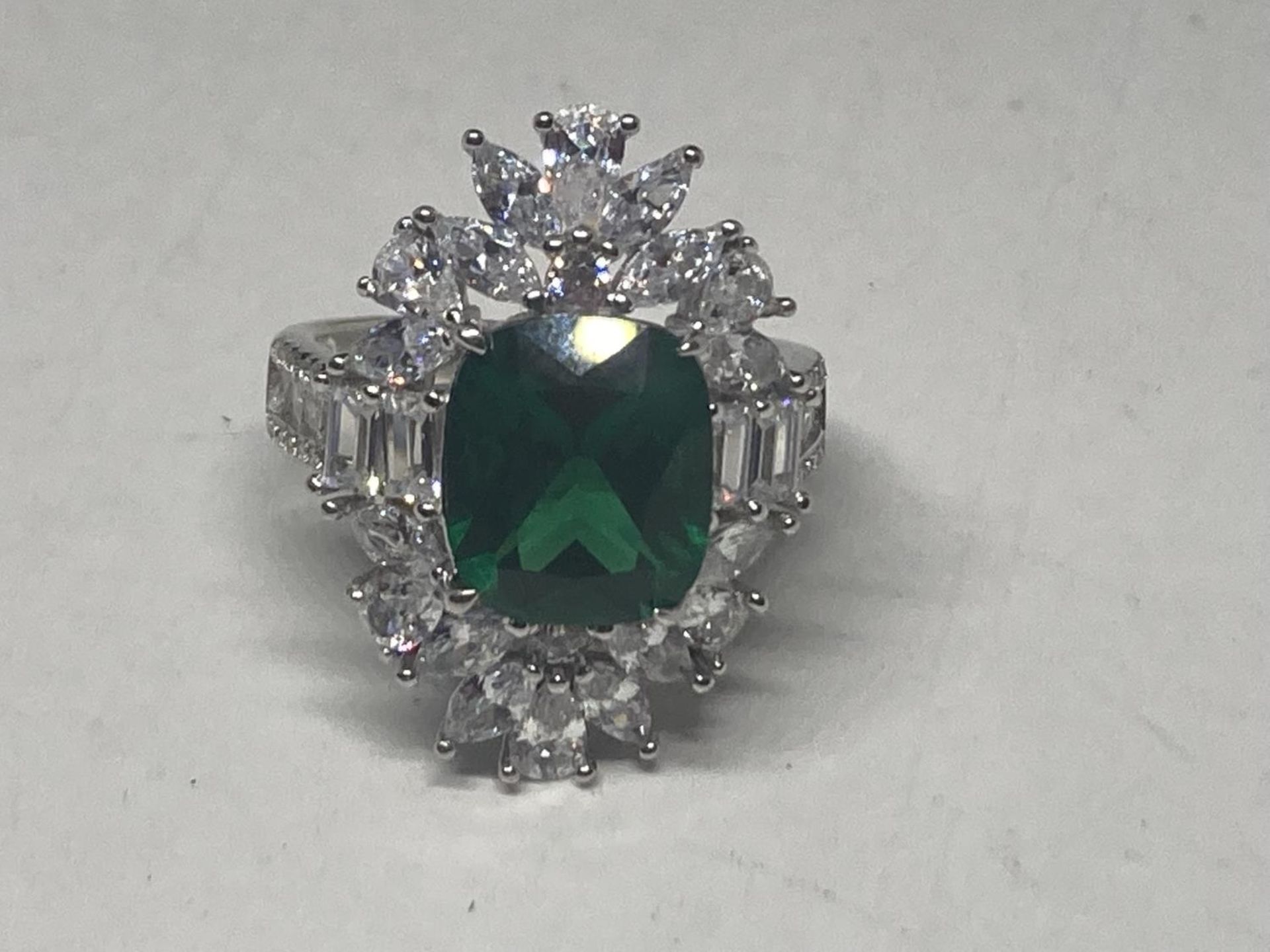 A WHITE METAL RING WITH A LARGE CENTRE LABORATORY GROWN EMERALD SURROUNDED BY CLEAR STONES SIZE S