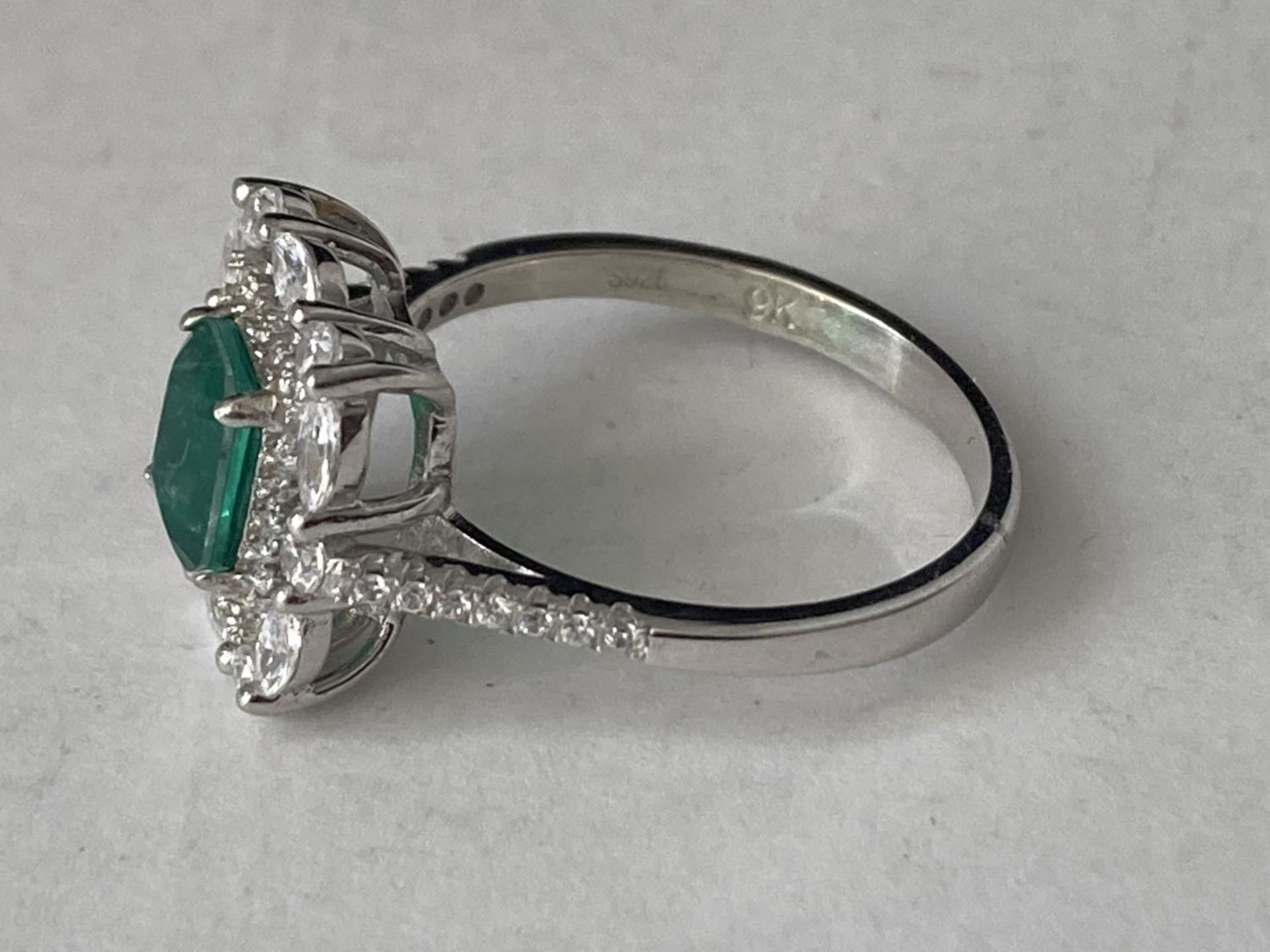 A WHITE METAL RING WITH A CENTRE RECTANGULAR LABORATORY GROWN EMERALD SURROUNDED BY CLEAR STONES - Image 3 of 6