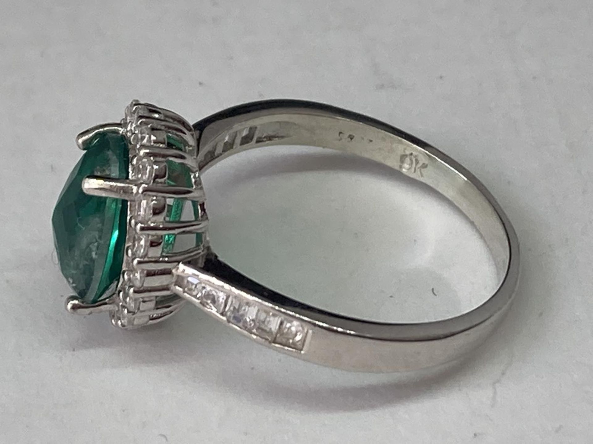 A WHITE METAL RING WITH A CENTRE LABORATORY GROWN EMERALD WITH CLEAR STONES SURROUNDING AND ON THE - Image 3 of 6