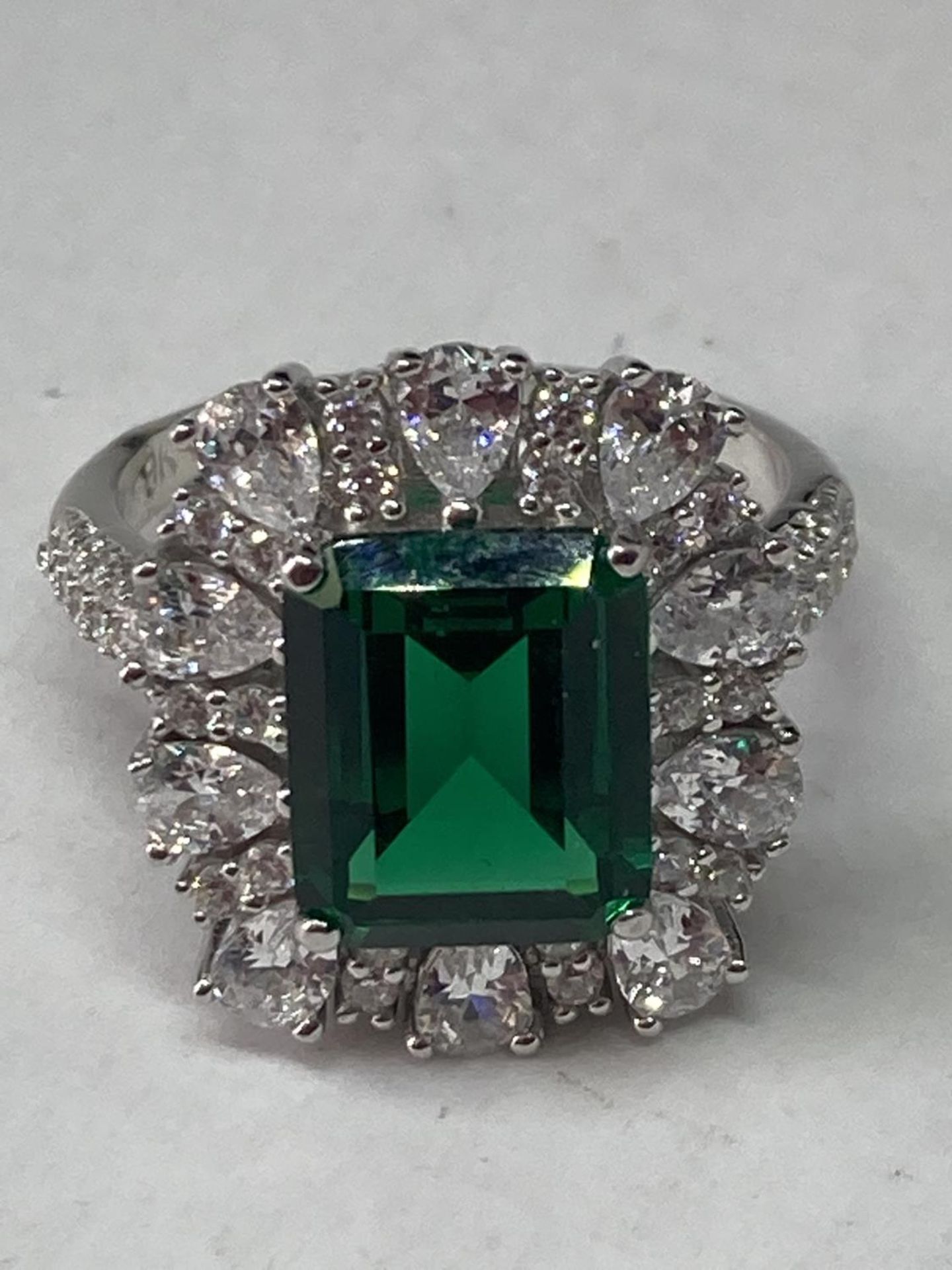 A WHITE METAL RING WITH A LARGE RCTANGULAR LABORATORY EMERALD SURROUNDED BY CLEAR STONES ALSO ON THE - Image 2 of 8