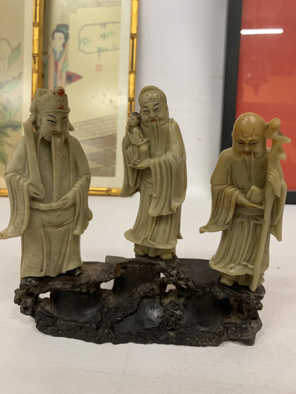 A FINE CHINESE CARVED SOAPSTONE FIGURE GROUP OF THREE IMMORTALS MOUNTED ON A CARVED STAND