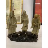 A FINE CHINESE CARVED SOAPSTONE FIGURE GROUP OF THREE IMMORTALS MOUNTED ON A CARVED STAND