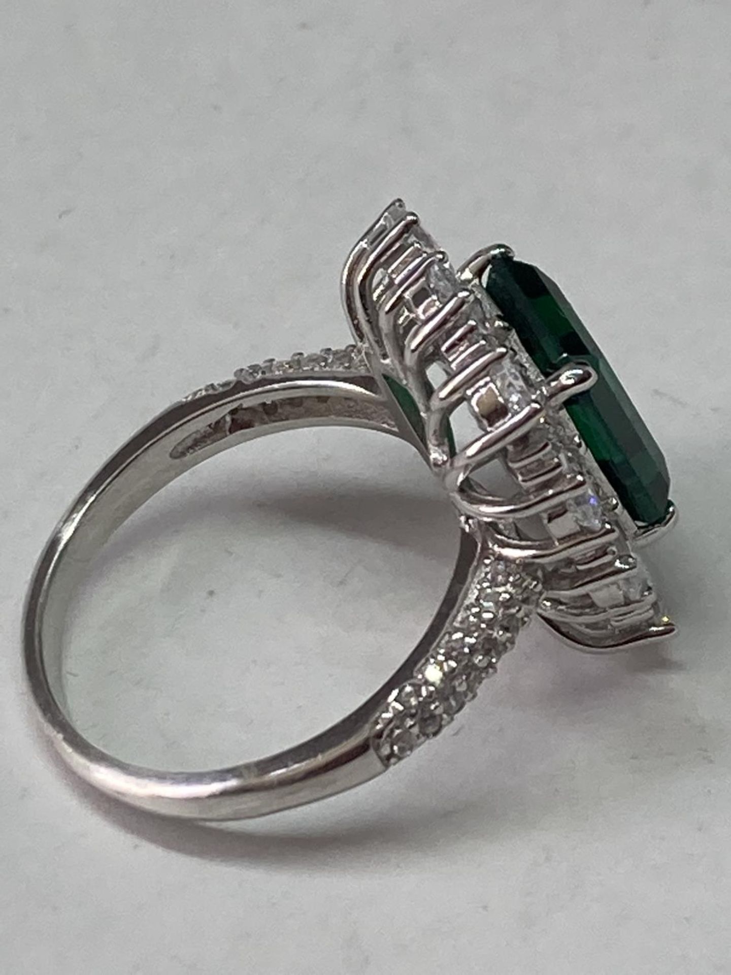 A WHITE METAL RING WITH A LARGE RCTANGULAR LABORATORY EMERALD SURROUNDED BY CLEAR STONES ALSO ON THE - Image 6 of 8