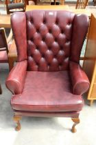 AN OX BLOOD EFFECT WINGED LOUNGE CHAIR ON FRONT CABRIOLE LEGS