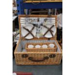A LARGE WICKER PICNIC HAMPER CONTAINING CERAMIC CUPS AND PLATES, PLUS CUTLERY, A BOTTLE OPENER AND