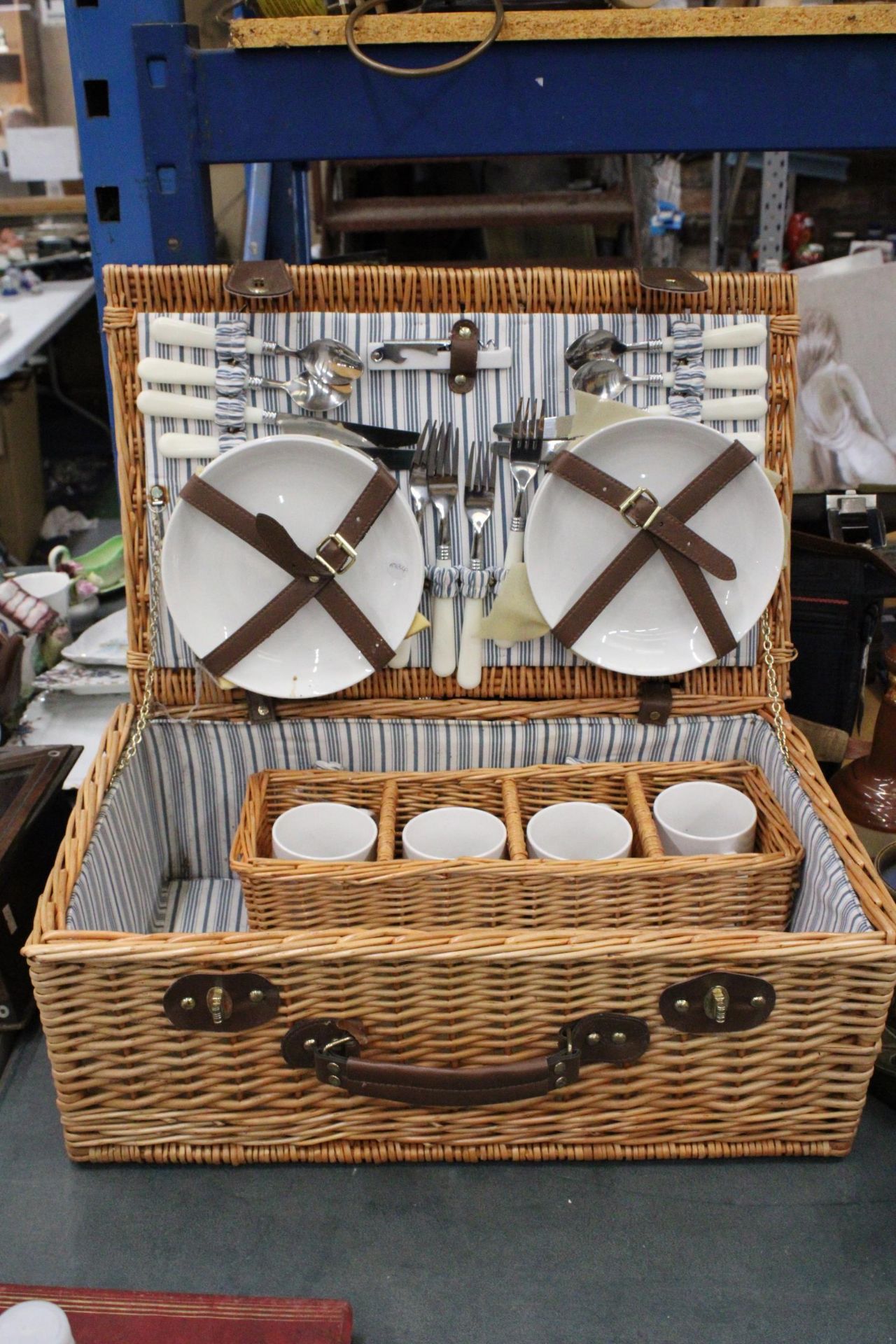 A LARGE WICKER PICNIC HAMPER CONTAINING CERAMIC CUPS AND PLATES, PLUS CUTLERY, A BOTTLE OPENER AND