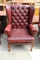 AN OX BLOOD EFFECT WINGED LOUNGE CHAIR ON FRONT CABRIOLE LEGS