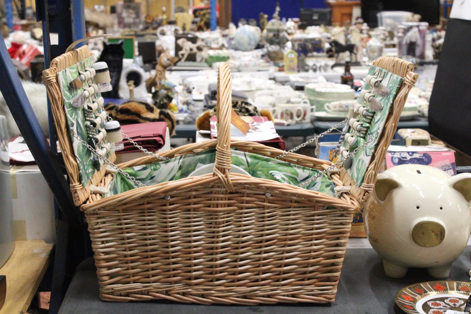 A WICKER PICNIC BASKET WITH LEAF PATTERN INTERIOR TO INCLUDE KNIVES, FORKS, SPOONS, PLATES, SALT AND