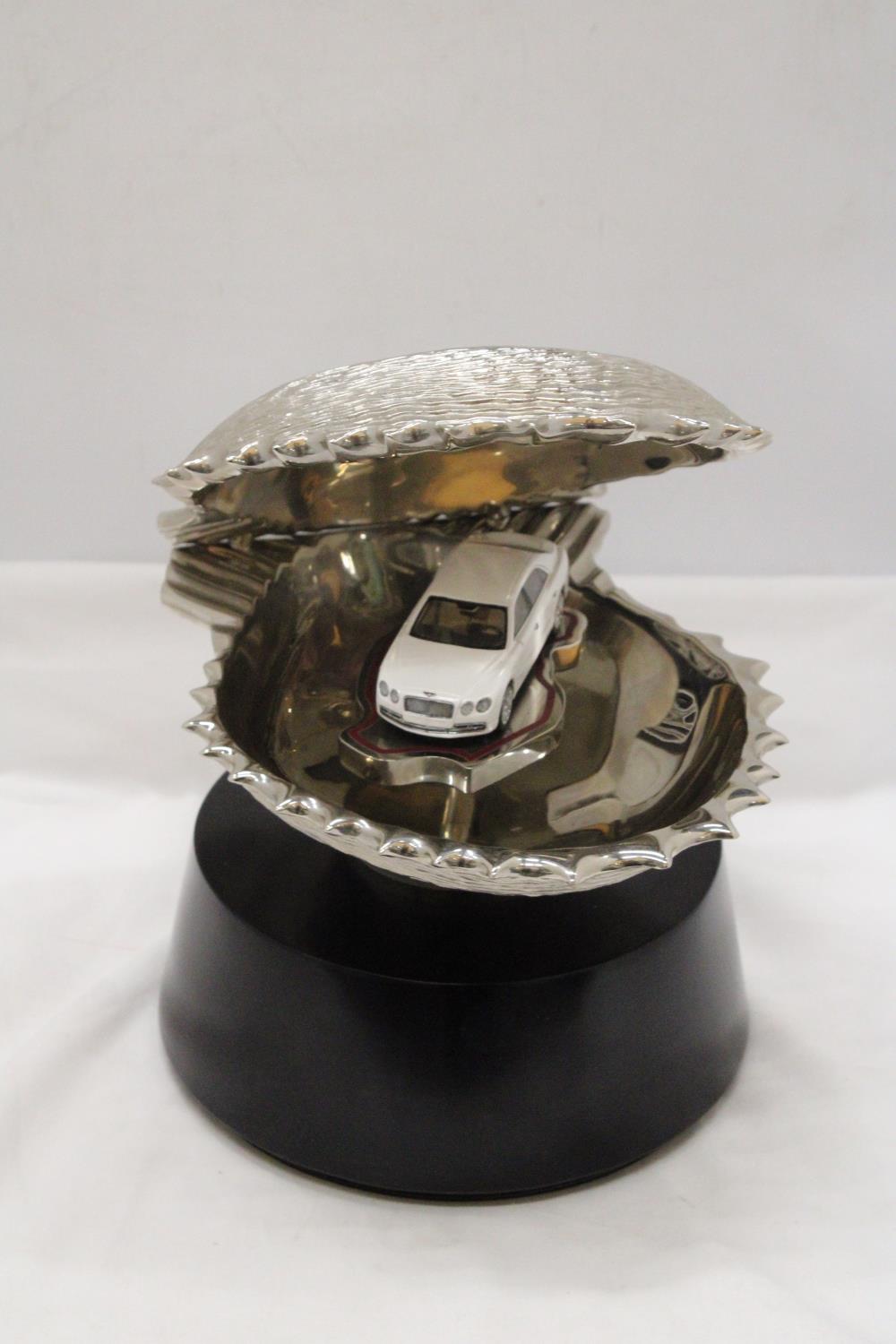 A LARGE CHROME OYSTER SHELL, ENCLOSING A BENTLEY CAR, ON A BASE, HEIGHT 30CM, DIAMETER APPROX 24CM