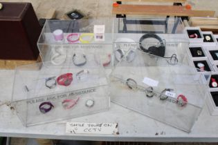 FOUR PLASTIC DISPLAY STANDS WITH AN ASSORTMENT OF FASHION WATCHES AND HEADPHONES