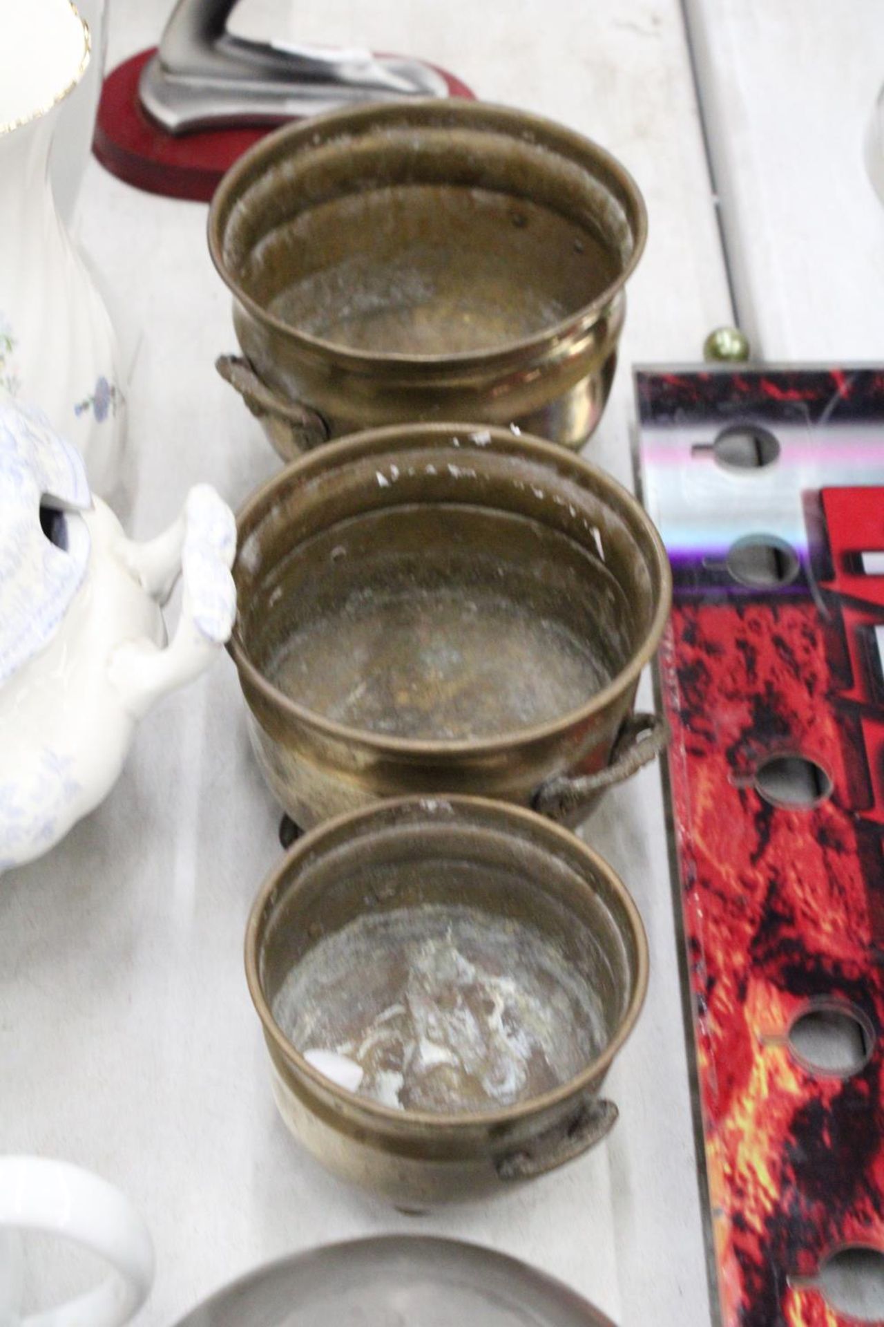 THREE GRADUATED BRASS FOOTED AND HANDLED POTS