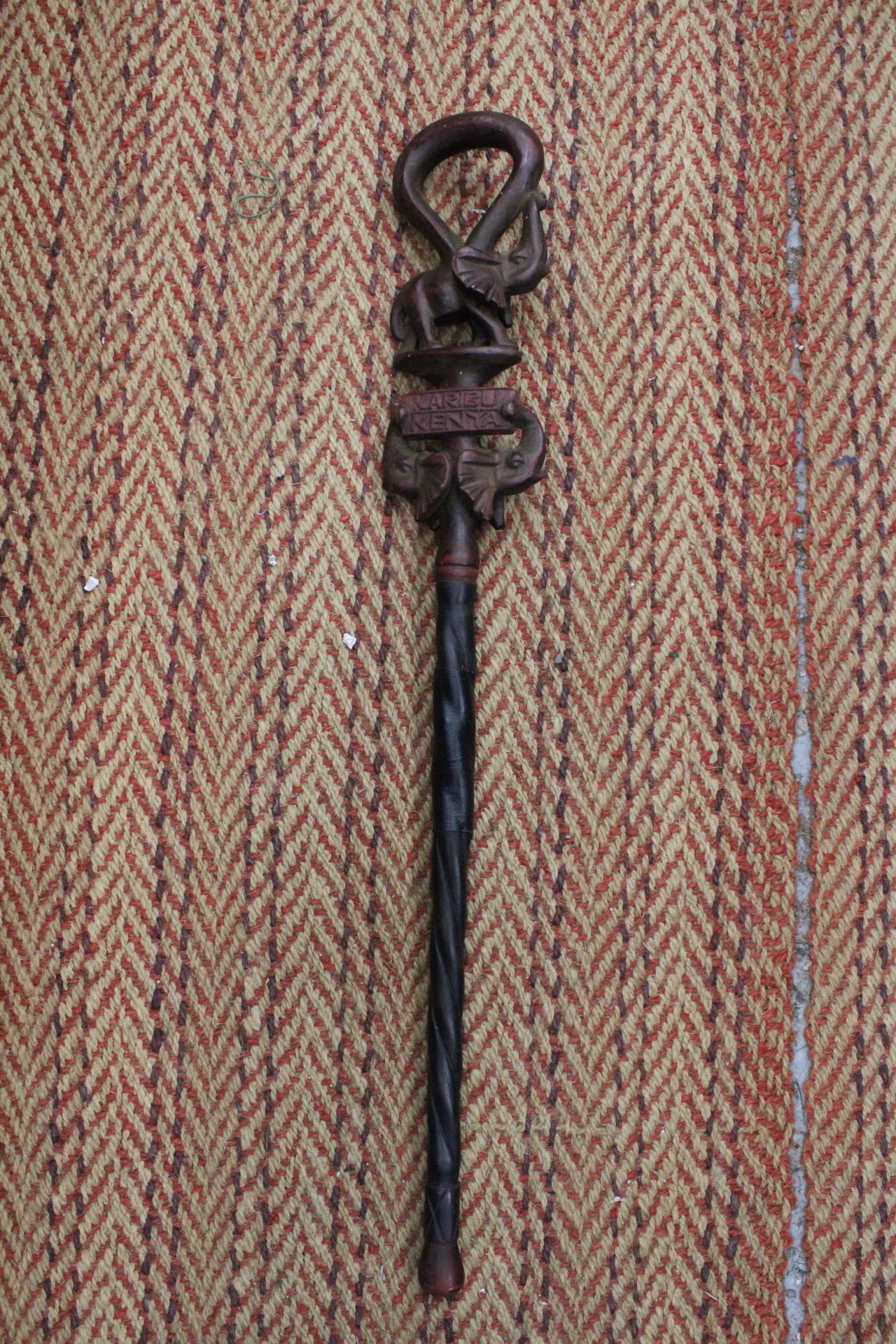 A HAND CARVED AFRICAN WALKING STICK, WITH ELEPHANT FIGURES TO THE TOP, WITH THE INSCRIPTION 'KARIBU,