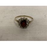 A 9 CARAT GOLD RING WITH CENTRE GARNET SURROUNDED BY CUBIC ZIRCONIAS SIZE U/V