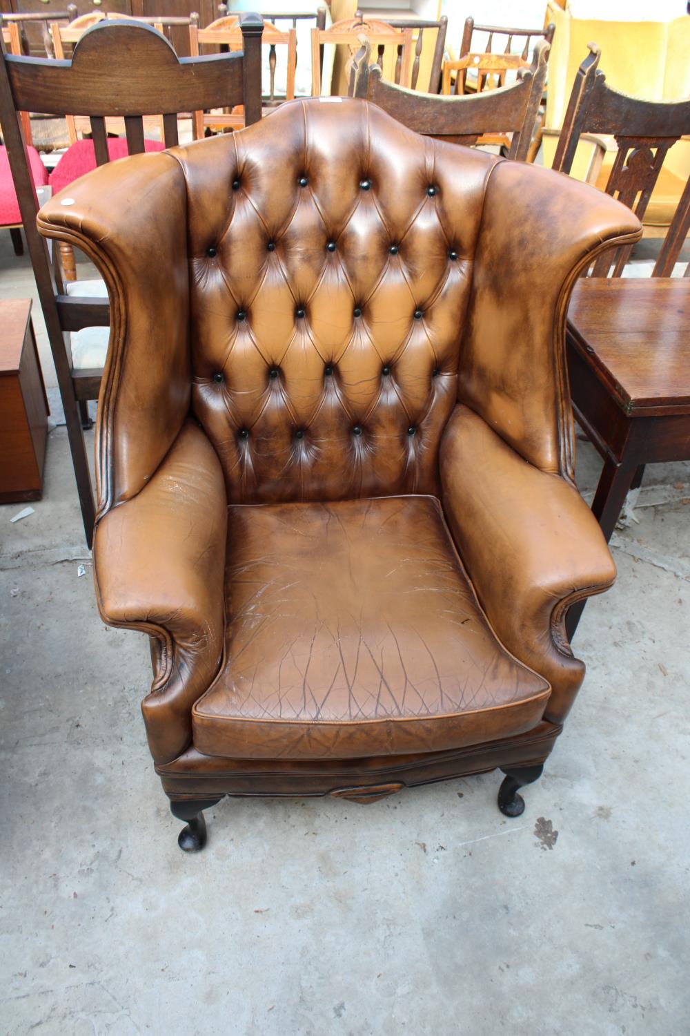 A BROWN CHESTERFIELD STYLE WINGED FIRESIDE CHAIR ON FRONT CABRIOLE LEGS