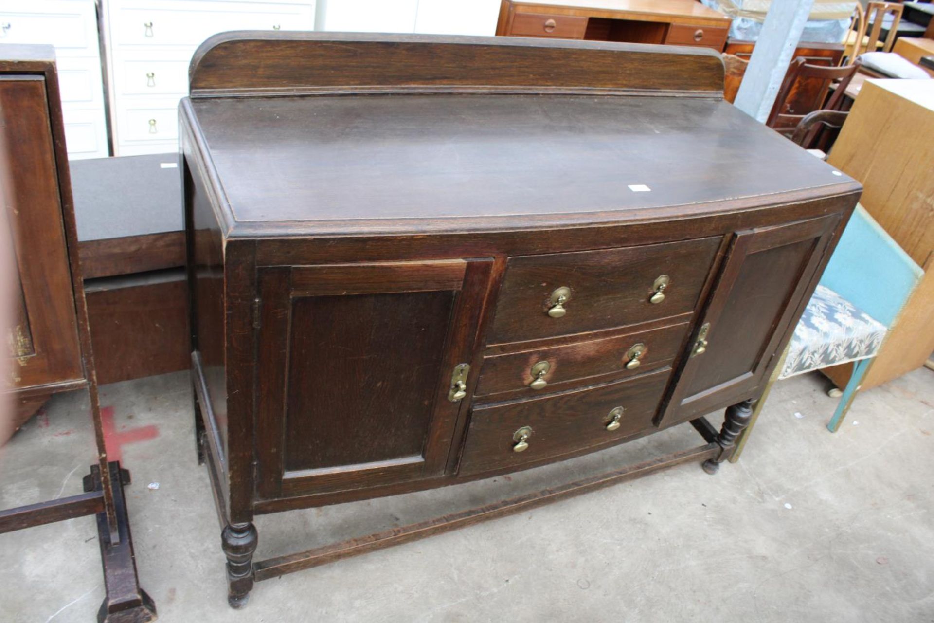 A MID 20TH CENTURY OAK SIDEBOARD ON OPEN BASE WITH TURNED LEGS ENCLOSING TWO CUPBOARDS AND THREE