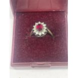 A SILVER RING WITH CENTRE RED STONE SURROUNDED BY CLER STONES IN A PRESENTATION BOX