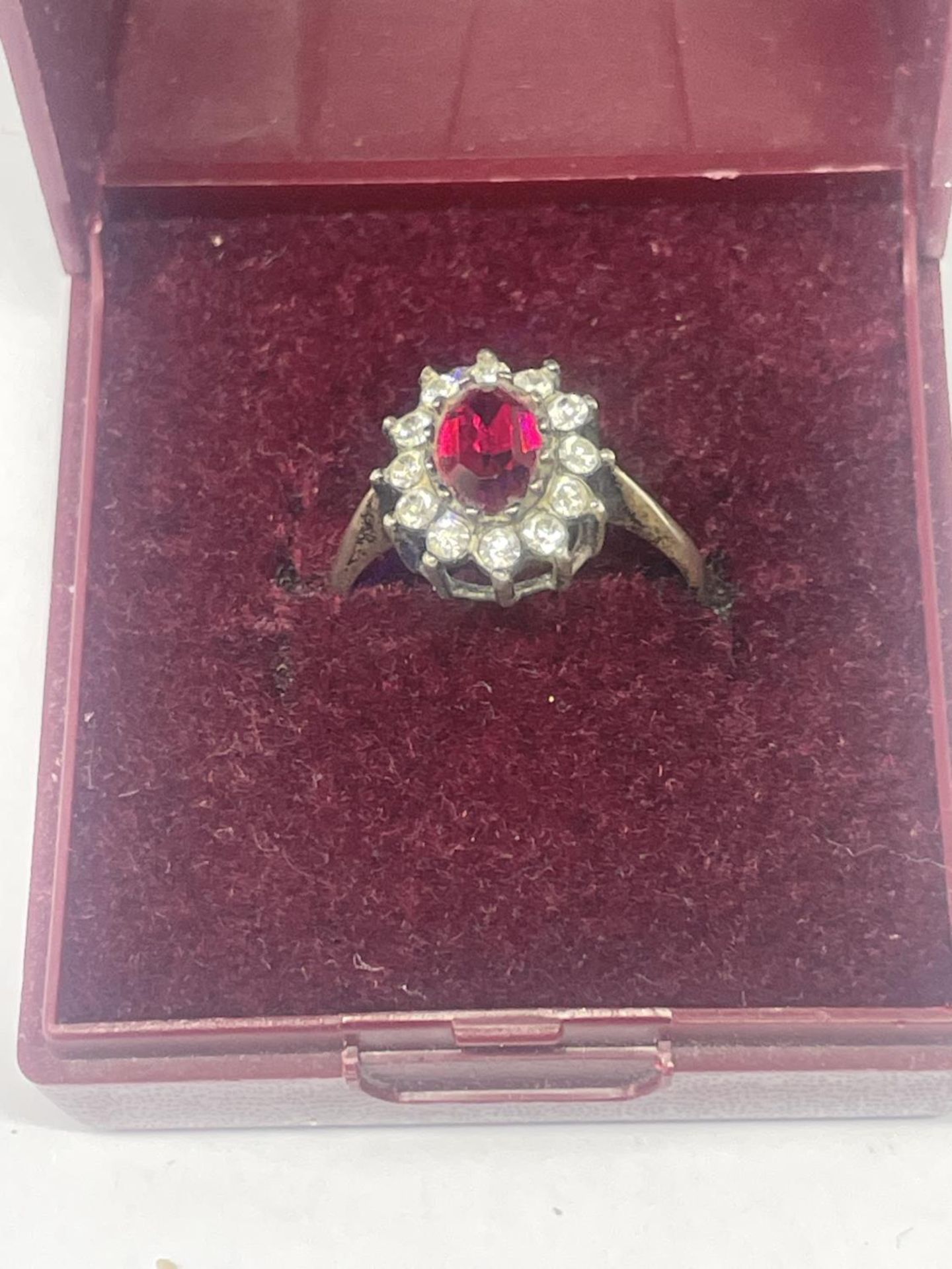 A SILVER RING WITH CENTRE RED STONE SURROUNDED BY CLER STONES IN A PRESENTATION BOX