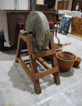 A weathered mill wheel grindstone on wooden stand - length 102cm, height 109cm