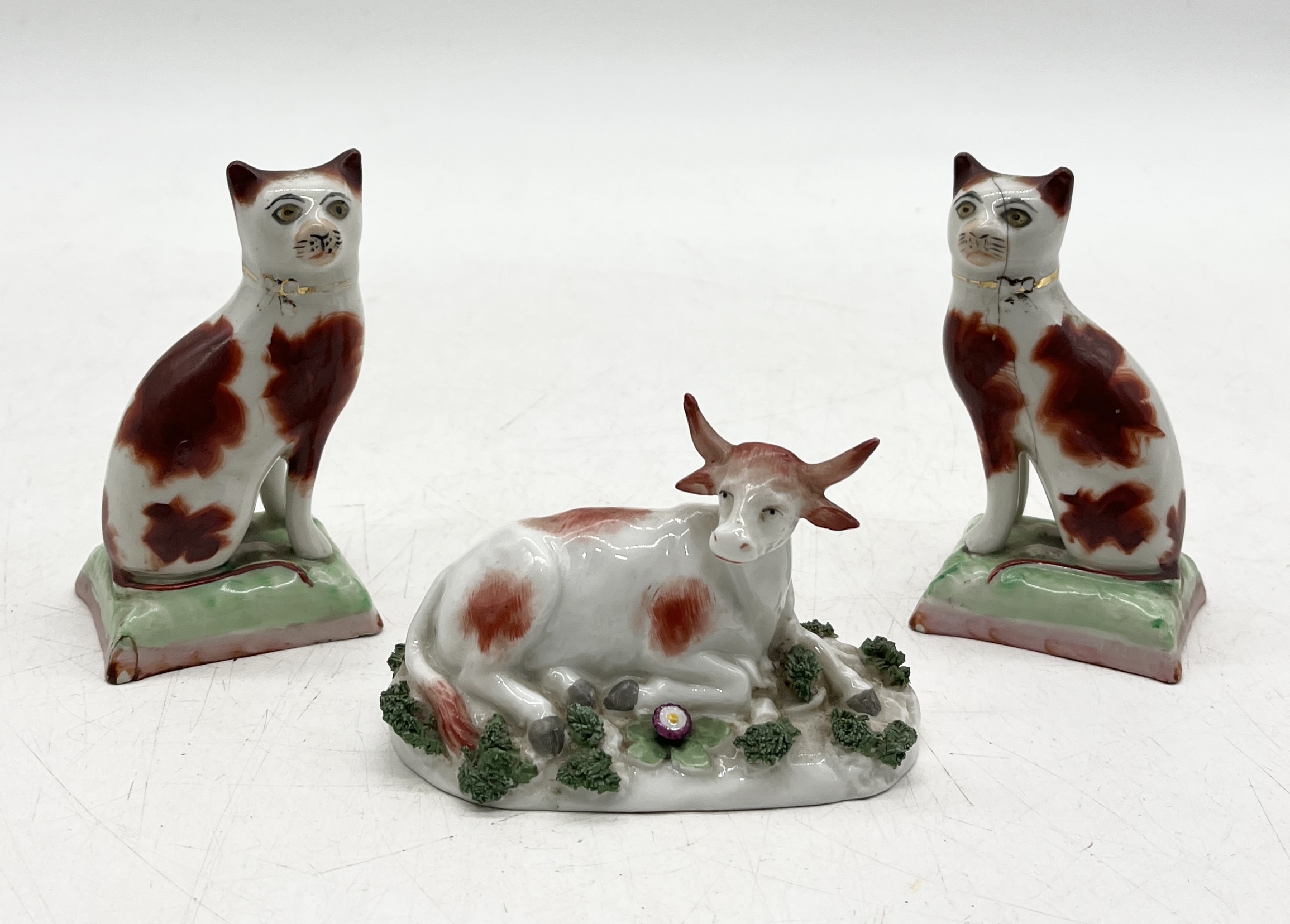 A small Staffordshire figure of a cow along with a pair of Staffordshire cats (1 A/F)