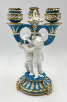 A Mintons three branch candelabra supported by three cherubs with blue and gilt detail - 28cm high