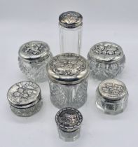 A collection of 7 silver topped dressing table pots all decorated with cherubs
