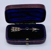 An unmarked rose gold (tested 9ct) brooch in the form of an arrow set with diamonds and a sapphire