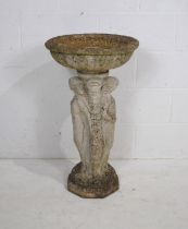 A weathered reconstituted stone bird bath, the base in the form of three classical ladies -