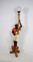 A painted and gilded wooden standard lamp in the form of a Blackmoore figure, holding a light with