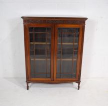 A turn of the century mahogany display cabinet, with carved detailing and astragal glazing, raised