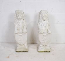 A pair of white painted reconstituted stone garden lions upon shields - length 24cm, height 81cm