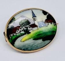 A continental porcelain plaque brooch set in unmarked 9ct gold depicting a village scene