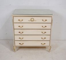 A French style white painted chest of five drawers, with glass top and gilded decoration, raised