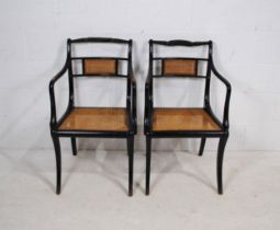 A pair of Regency style ebonised carver chairs, with cane seats