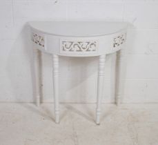 A white painted demi-lune table, with carved and pierced decoration, raised on turned legs -