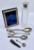 A small silver photo frame, silver topped scent bottle and three silver spoons