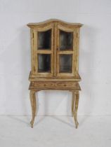 A rustic painted display cabinet of small proportions, with single drawer, raised on French cabriole