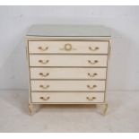 A French style white painted chest of five drawers, with glass top and gilded decoration, raised