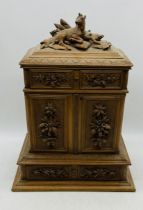 A Black Forest style table top cabinet with six drawers, carved detailing and seated dear finial -