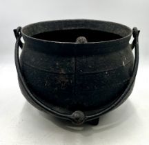 A vintage cast iron cauldron on tripod legs with tongs