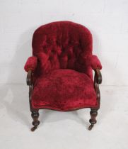 A Victorian button-back armchair, raised on turned legs with brass castors