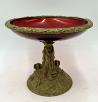 A ruby glass tazza with brass rim and base in the form of three stylised dolphins