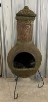 A weathered terracotta chiminea on wrought iron tripod stand