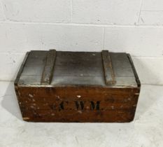 A large ammo crate with C.W.M stenciled onto sides, one side part painted, with two metal brackets
