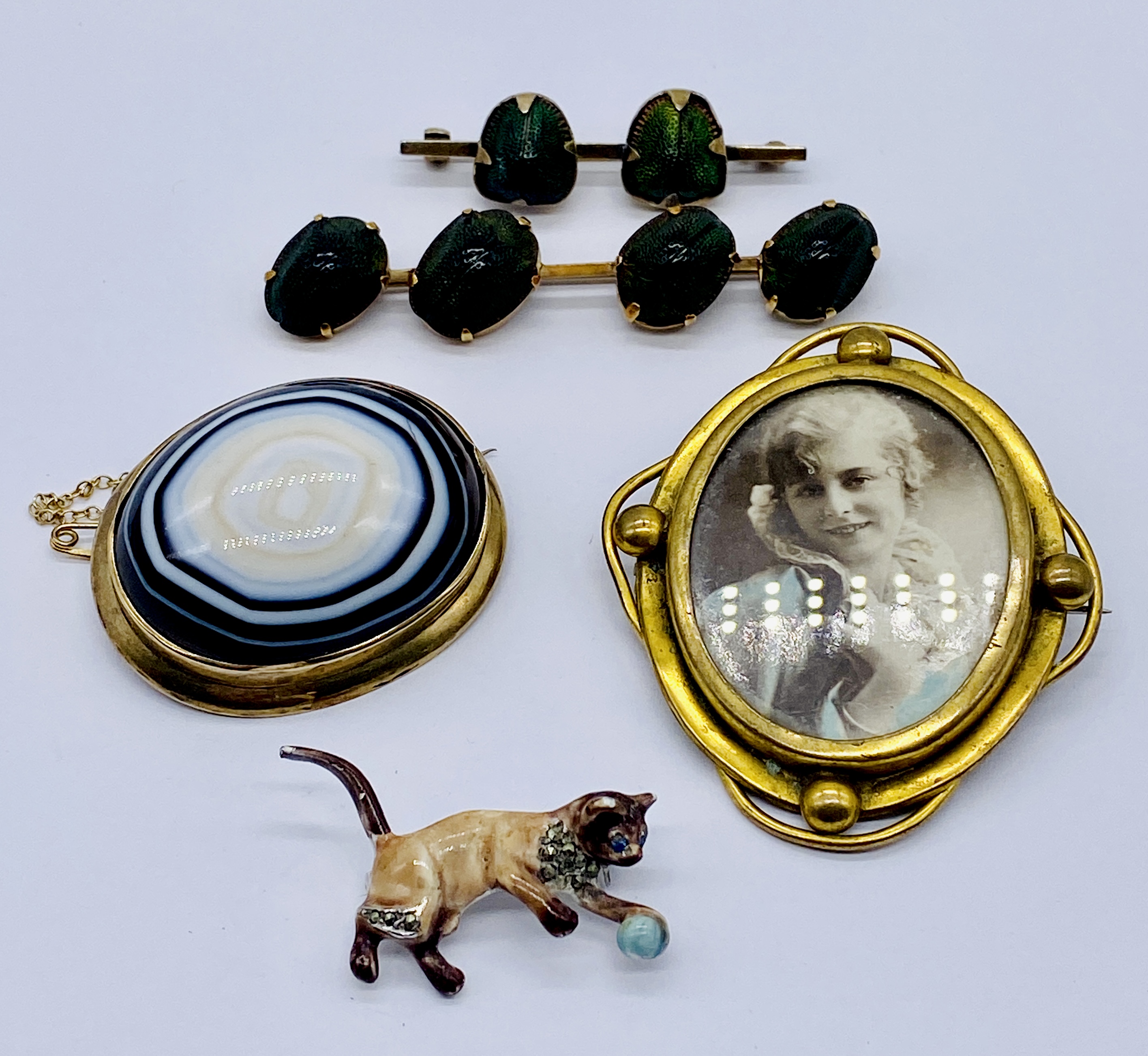 A Victorian yellow metal brooch set with a large banded agate, scarab brooches, enamelled cat brooch