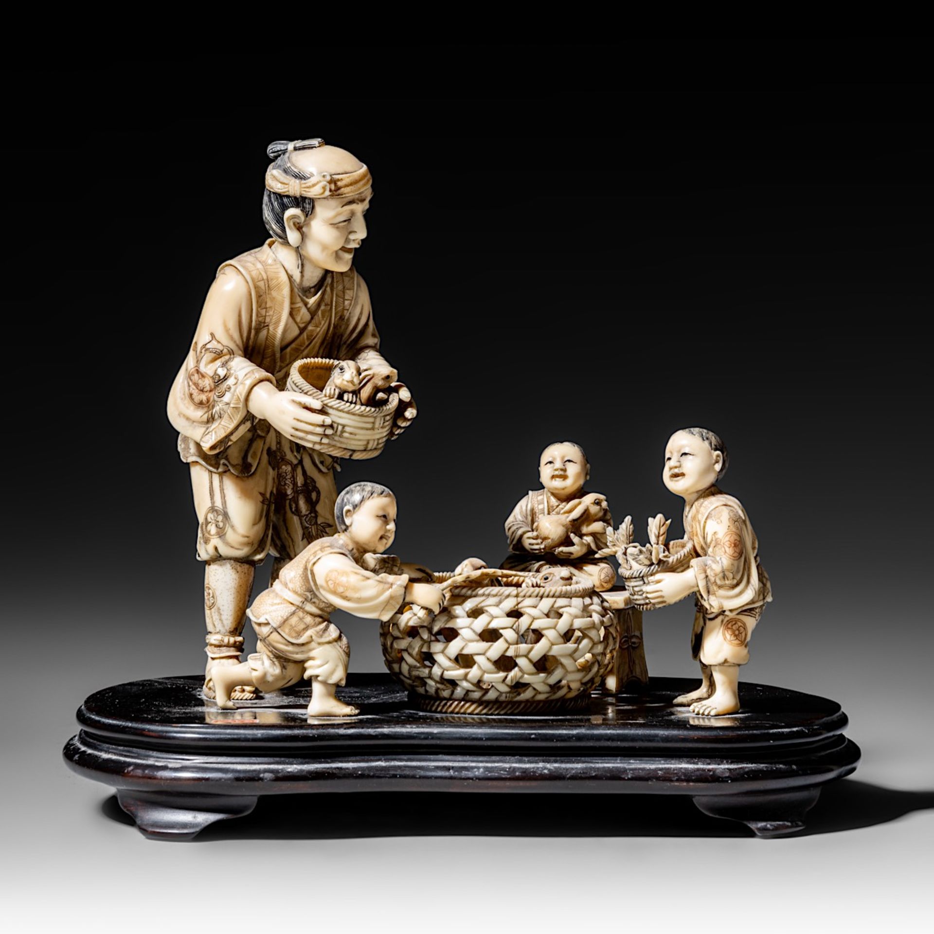 A walrus/sperm whale ivory okimono group of a family with bunnies, fixed on a black lacquered wooden