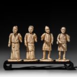 Four Japanese bone okimono, the figures possibly representing different classes in society, on a woo
