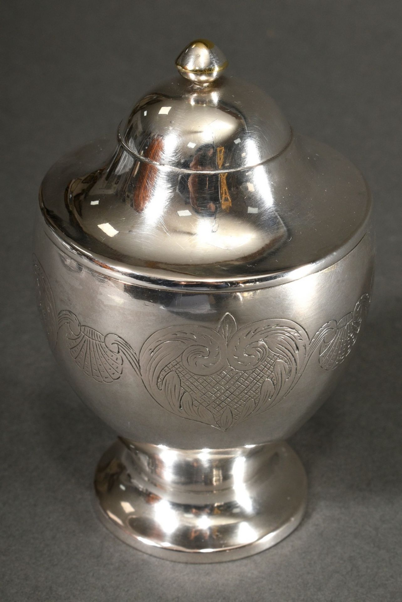 An urn-shaped lidded box on a round foot with delicately engraved shell and leaf border, slightly d