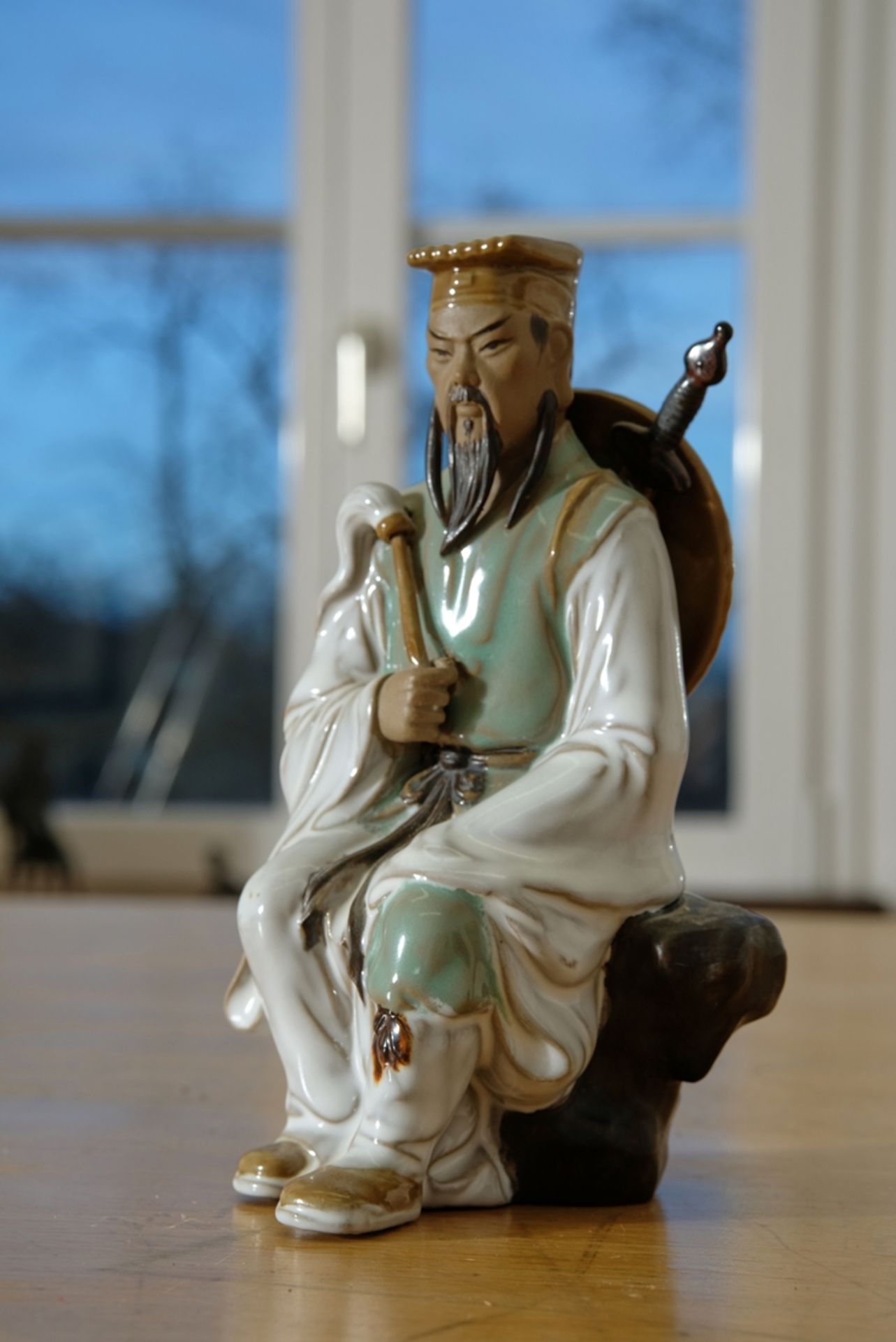 Warrior figure, Chinese. Ceramic. Sitting warrior, carrying sword and shield on his back, holding a
